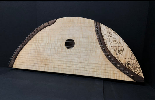 A handmade wooden stringed instrument, a Baltic Psaltry, featuring a light natural maple top, dark brown decorative borders, and intricate floral carvings on the right side, set against a dark background.